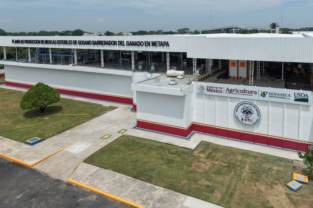 Fachada de la planta de producción de moscas estériles con logotipos de México, Agricultura, Senasica y USDA.
