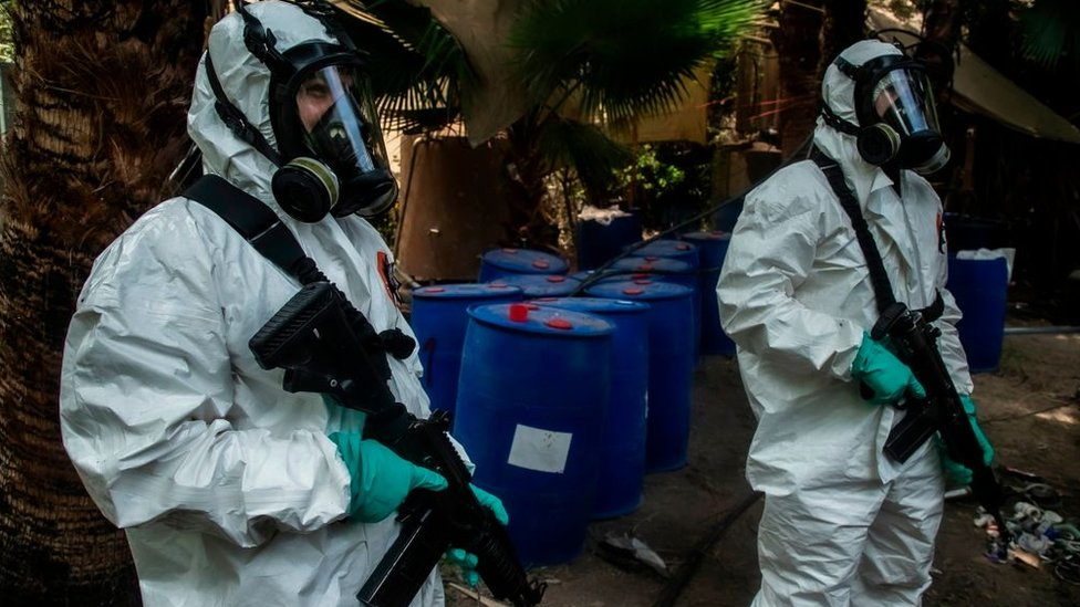 Agentes con trajes de protección y máscaras antigás revisan contenedores químicos en un posible laboratorio clandestino.