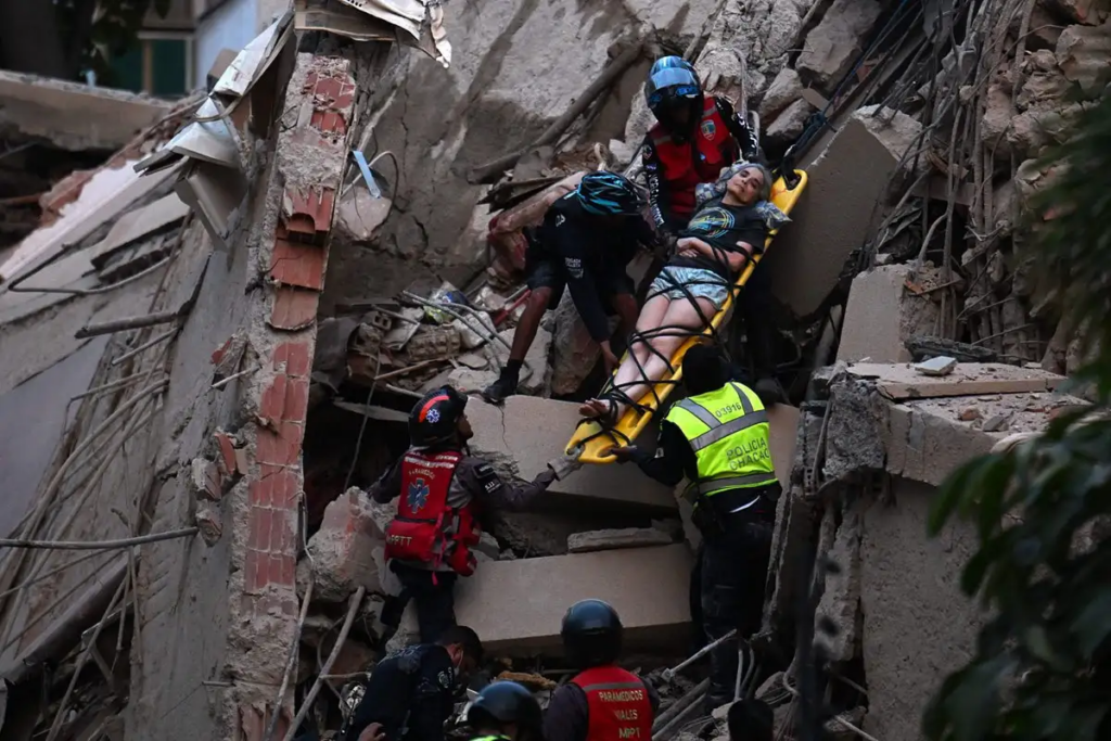 Equipos de rescate trasladan en camilla a una mujer herida entre los restos de un edificio colapsado.