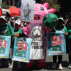 Persona disfrazada de axolotl con la leyenda México Crisis Forense, rodeada de carteles estilo carta FIFA con fotos de personas desaparecidas en Ecatepec