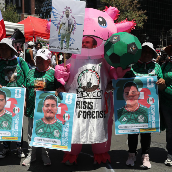 Persona disfrazada de axolotl con la leyenda México Crisis Forense, rodeada de carteles estilo carta FIFA con fotos de personas desaparecidas en Ecatepec