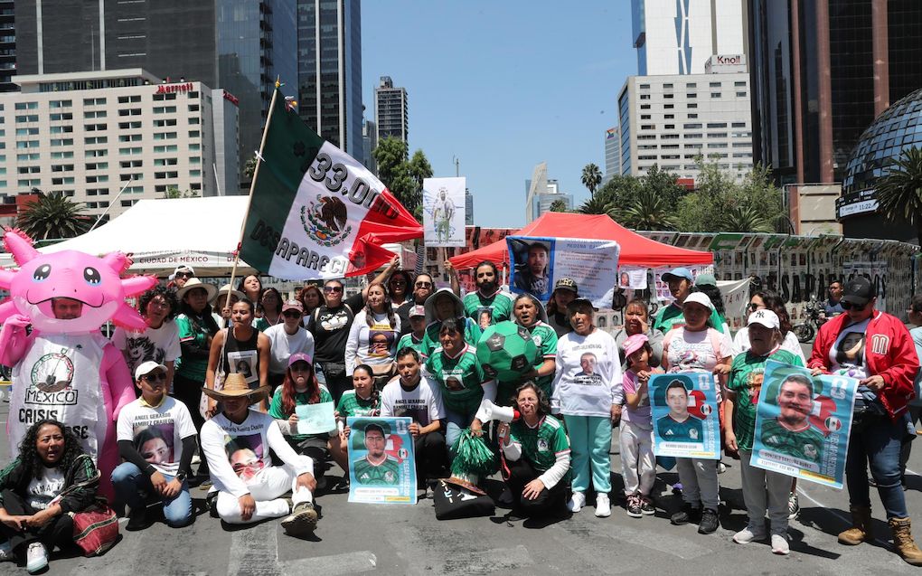 Persona disfrazada de axolotl con la leyenda México Crisis Forense, rodeada de carteles estilo carta FIFA con fotos de personas desaparecidas en Ecatepec