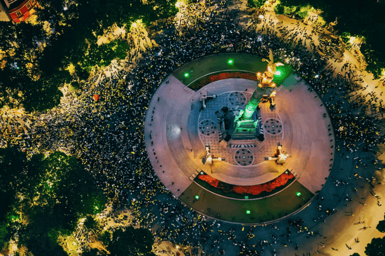 Vista aérea nocturna del Ángel de la Independencia rodeado por una multitud que celebra el pase de México a octavos de final del Mundial 2026
