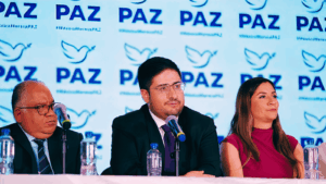 Dirigentes de Partido PAZ durante una conferencia con el logotipo del nuevo instituto político al fondo.