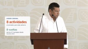 Javier May durante una conferencia; el visual informa ocho actividades semanales y ocho recorridos por los 17 municipios de Tabasco.