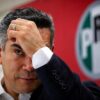 Alejandro Moreno, dirigente nacional del PRI, se lleva una mano a la frente frente al emblema de su partido.