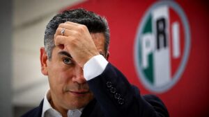 Alejandro Moreno, dirigente nacional del PRI, se lleva una mano a la frente frente al emblema de su partido.
