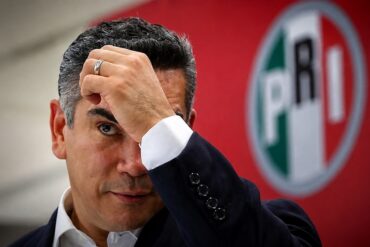 Alejandro Moreno, dirigente nacional del PRI, se lleva una mano a la frente frente al emblema de su partido.