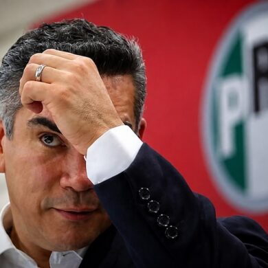 Alejandro Moreno, dirigente nacional del PRI, se lleva una mano a la frente frente al emblema de su partido.