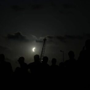 Siluetas de observadores contemplan una fase avanzada del eclipse solar de 2026 en la península ibérica.