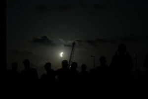Siluetas de observadores contemplan una fase avanzada del eclipse solar de 2026 en la península ibérica.