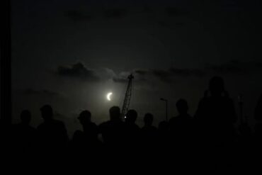 Siluetas de observadores contemplan una fase avanzada del eclipse solar de 2026 en la península ibérica.