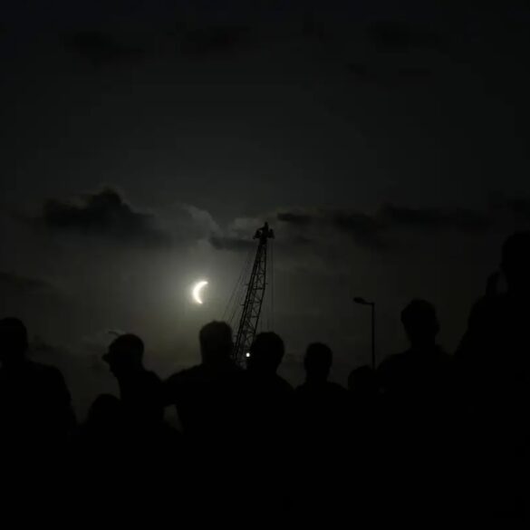 Siluetas de observadores contemplan una fase avanzada del eclipse solar de 2026 en la península ibérica.