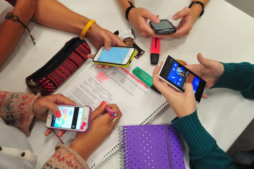 Estudiantes utilizan teléfonos celulares junto con cuadernos y materiales durante una actividad escolar