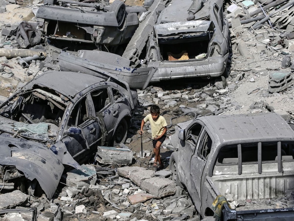 Un niño camina entre autos destruidos y escombros en Gaza