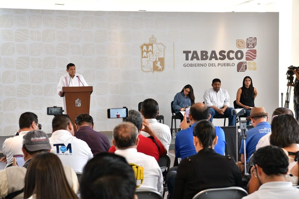 Conferencia de prensa del gobernador Javier May Rodríguez en Villahermosa, con reporteros en primer plano y el logotipo del Gobierno de Tabasco al fondo