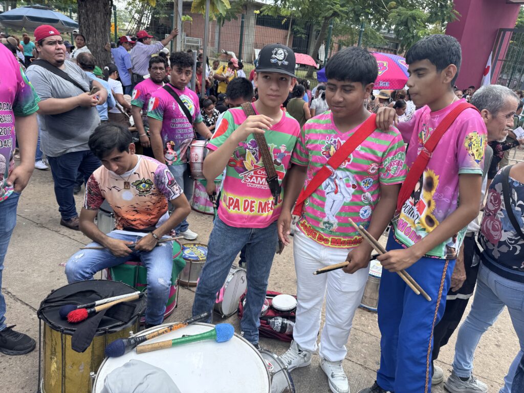 Jóvenes de la batucada Choco Samba, de Jalpa de Méndez, con playeras rosas y verdes y sus tambores en la entrada del estadio.