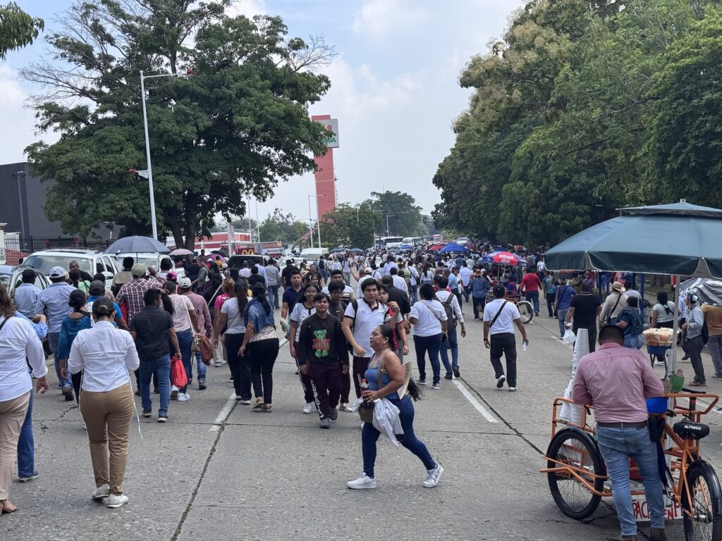 Cientos de personas caminando por una avenida arbolada a la salida del evento en la Ciudad Deportiva de Villahermosa.