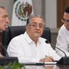 Composición visual de tres funcionarios y actores políticos en una mesa de sesión, con el secretario Ejecutivo del órgano electoral al centro bajo presión política.