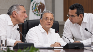Composición visual de tres funcionarios y actores políticos en una mesa de sesión, con el secretario Ejecutivo del órgano electoral al centro bajo presión política.