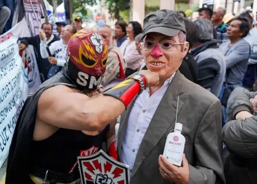 Manifestante vestido de luchador con la leyenda SME golpea a otro que usa una máscara de Calderón
