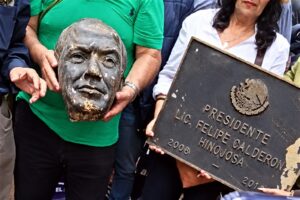 Manifestantes sostienen la cabeza de bronce de Felipe Calderón junto a la placa con la leyenda «Presidente Lic. Felipe Calderón Hinojosa 2006-2012»
