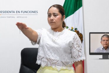 María Eliza Hernández Flores rinde protesta en primer plano, mientras Alfonso Baca aparece en una pantalla por su licencia temporal.