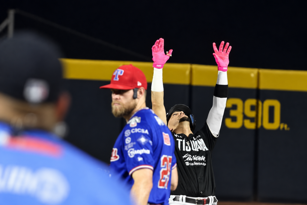 Jugador de Toros de Tijuana levanta los brazos mientras un pelotero de Olmecas aparece en primer plano.