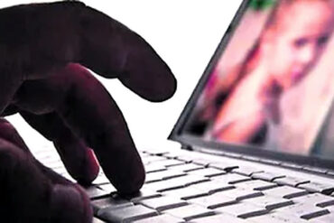Mano sobre el teclado de una computadora portátil con una imagen desenfocada en pantalla, ilustración de los delitos sexuales digitales.