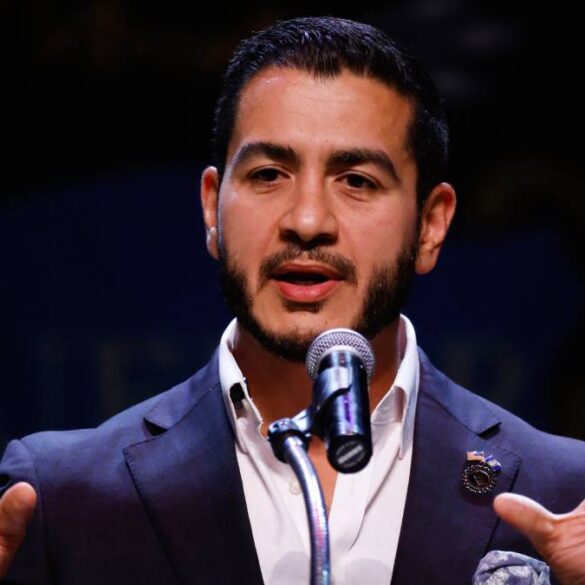 Abdul El-Sayed pronuncia un discurso ante un micrófono con ambas manos extendidas durante un acto público.