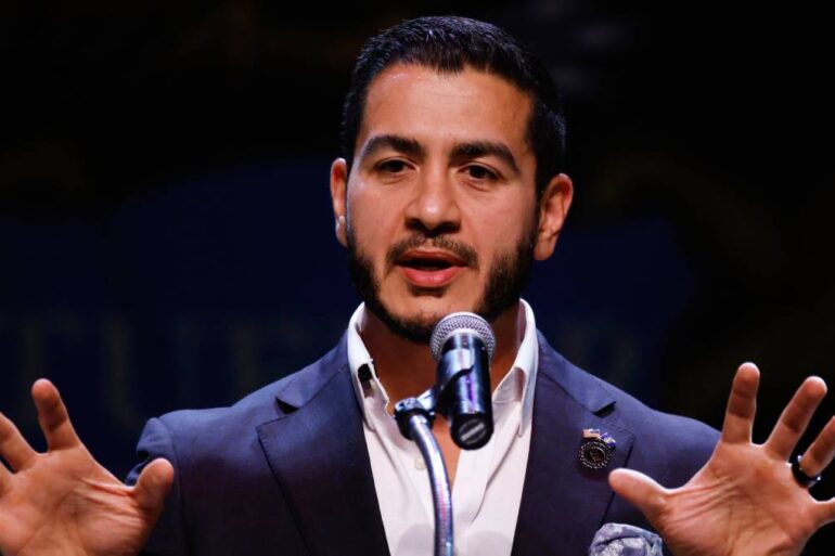 Abdul El-Sayed pronuncia un discurso ante un micrófono con ambas manos extendidas durante un acto público.