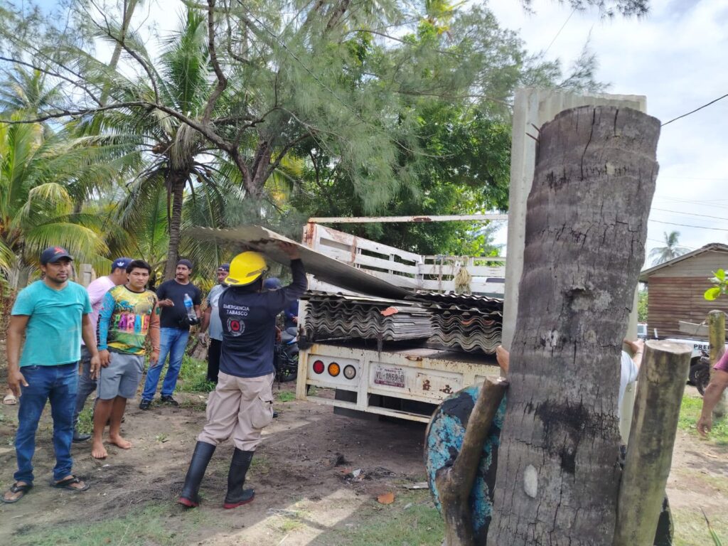 Personal de emergencia y habitantes colaboran en la carga de láminas sobre un camión en una comunidad de Tabasco afectada por el temporal.