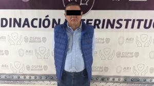 Persona presentada como detenida, con chaleco azul y ojos cubiertos por una franja negra, ante un fondo institucional en Chihuahua.