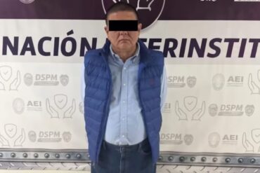 Persona presentada como detenida, con chaleco azul y ojos cubiertos por una franja negra, ante un fondo institucional en Chihuahua.