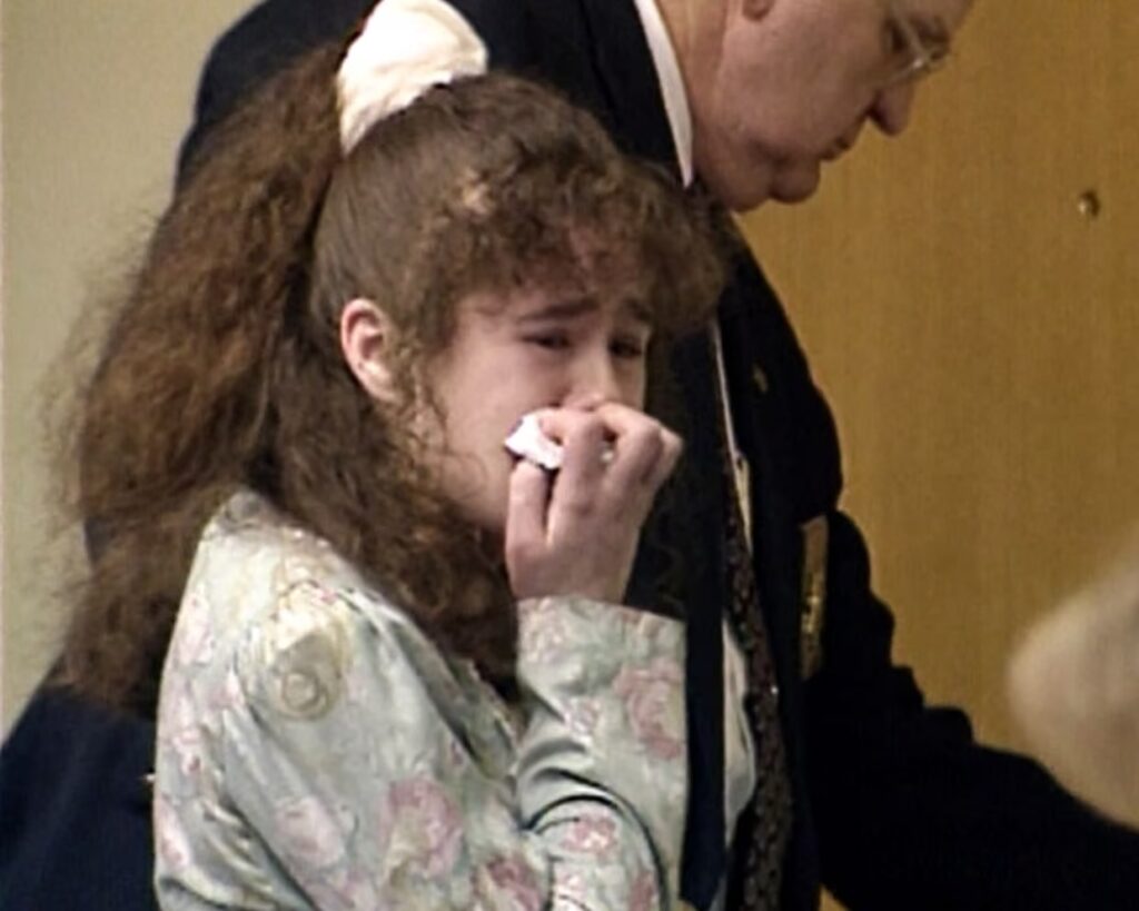 Christa Pike joven se cubre la boca con un pañuelo junto a un agente de traje, en una imagen de archivo