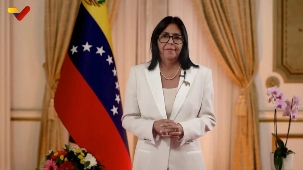 elcy Rodríguez, presidenta encargada de Venezuela, con traje blanco frente a la bandera venezolana en el Palacio de Miraflores