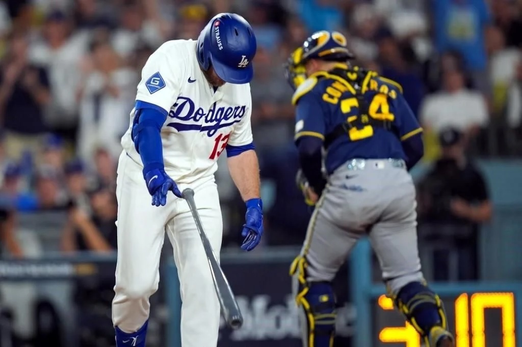 Bateador de Los Ángeles Dodgers permanece cabizbajo con el bate hacia abajo, mientras el receptor de Milwaukee se retira durante el partido de la Serie de Campeonato.