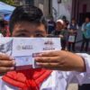 Estudiante con uniforme escolar muestra el sobre de su tarjeta del Banco del Bienestar, por donde se paga la beca Rita Cetina