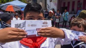 Estudiante con uniforme escolar muestra el sobre de su tarjeta del Banco del Bienestar, por donde se paga la beca Rita Cetina