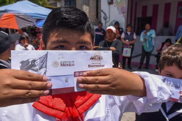 Estudiante con uniforme escolar muestra el sobre de su tarjeta del Banco del Bienestar, por donde se paga la beca Rita Cetina
