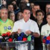 Flávio Bolsonaro lee un documento ante micrófonos de medios, rodeado de aliados con camisetas de su campaña, tras perder la segunda vuelta ante Lula
