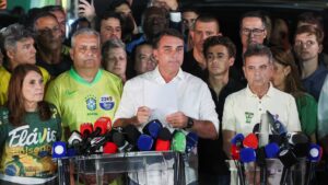 Flávio Bolsonaro lee un documento ante micrófonos de medios, rodeado de aliados con camisetas de su campaña, tras perder la segunda vuelta ante Lula