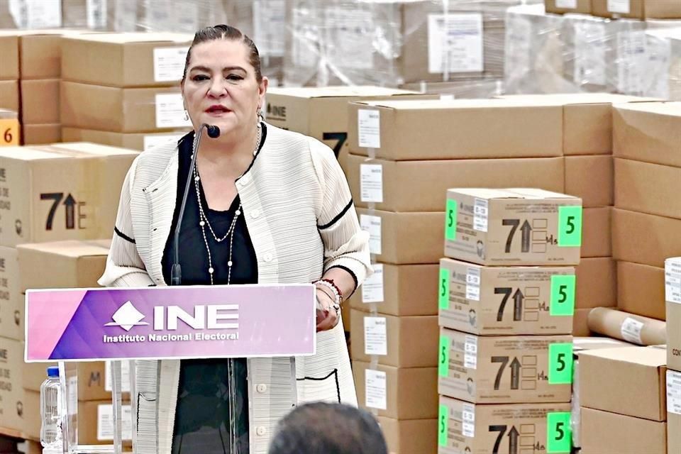 Guadalupe Taddei habla frente a paquetes y cajas de material electoral en instalaciones del INE.