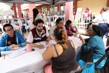 Servidores públicos del Gobierno de Tabasco atienden trámites de dos mujeres en una mesa durante una audiencia pública
