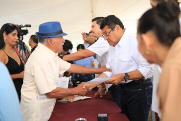 Javier May Rodríguez estrecha la mano de un vecino con sombrero azul durante la audiencia comunitaria 172 en Comalcalco, Tabasco
