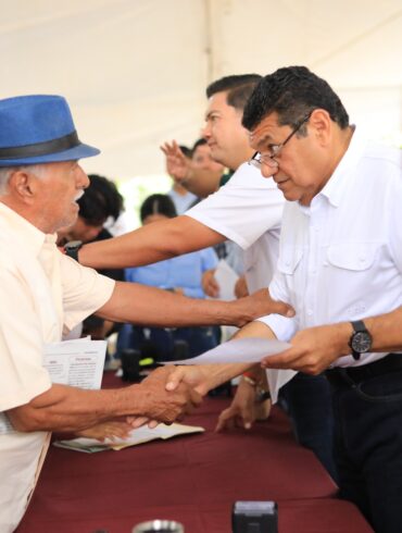 Javier May Rodríguez estrecha la mano de un vecino con sombrero azul durante la audiencia comunitaria 172 en Comalcalco, Tabasco