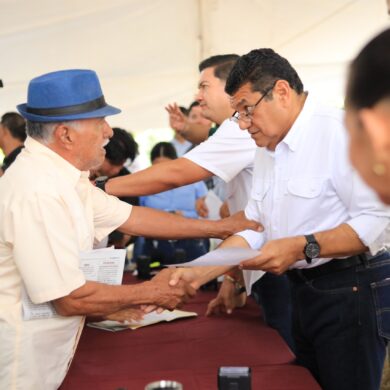 Javier May Rodríguez estrecha la mano de un vecino con sombrero azul durante la audiencia comunitaria 172 en Comalcalco, Tabasco