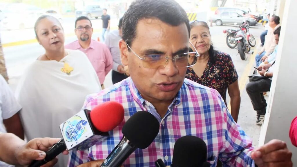 Jesús Selván García, con camisa de cuadros, responde a reporteros que le acercan varios micrófonos