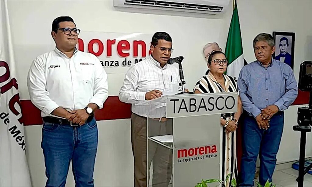 Jesús Selván García habla en un podio de Morena Tabasco, acompañado por tres integrantes del partido