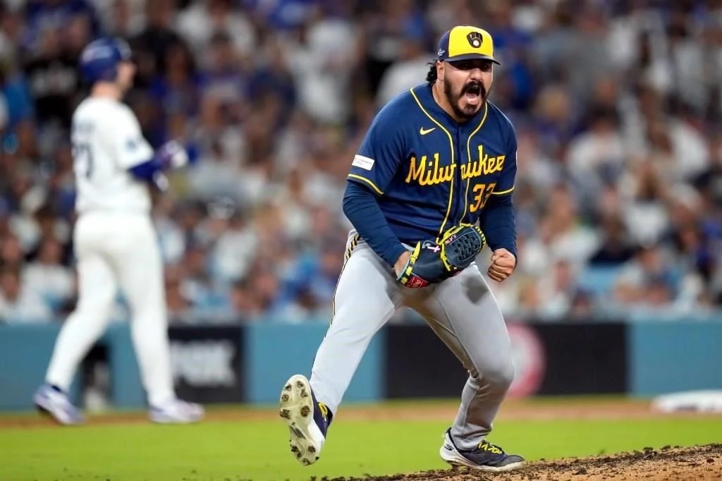 Lanzador de los Cerveceros de Milwaukee grita y aprieta el puño sobre el montículo, con un jugador de los Dodgers desenfocado al fondo.